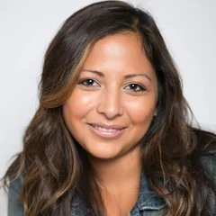 Professional headshot of a smiling woman with long dark hair wearing a denim jacket on a light background.
