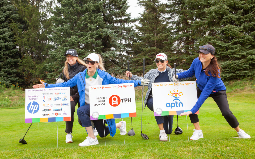 Four women pose with sponsor signs and golf clubs at the Drive for Dreams charity golf day.